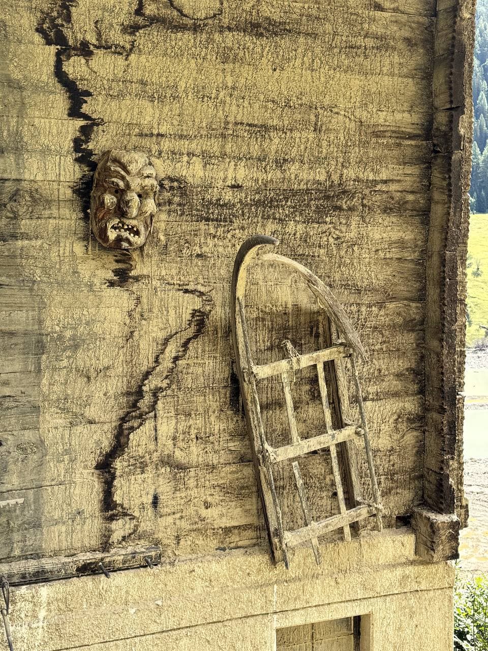 Geschnitzte Maske und alter Holzschlitten an einer Walliser Holzwand